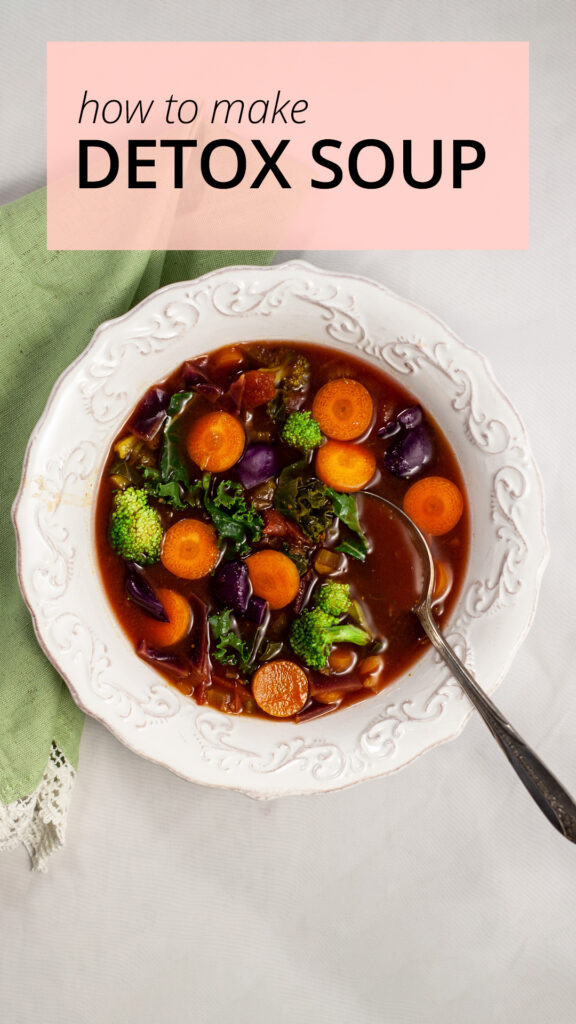 an overhead photo of a bowl of soup containing carrots, broccoli kale in a tomato broth. The bowl sits on a green napkin. A silver spoon sits inside the bowl.