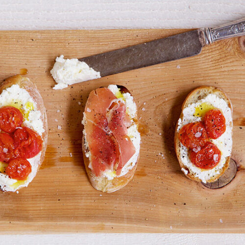 Overhead view of ricotta cheese on toast with tomatoes, prosciutto and flaky salt