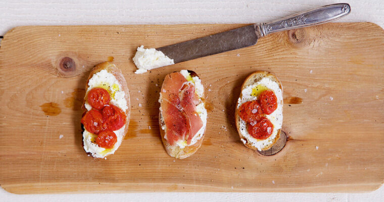 Overhead view of ricotta cheese on toast with tomatoes, prosciutto and flaky salt
