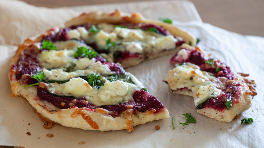 A photo of pizza topped with beet pesto, spinach, ricotta, mozzarella and chopped parsley.