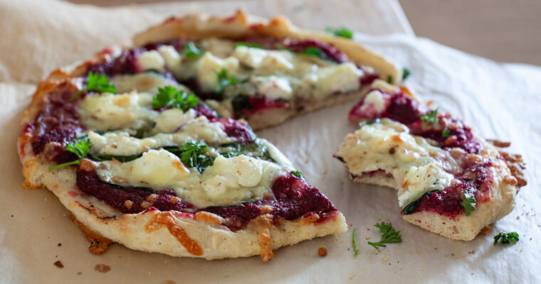 A photo of pizza topped with beet pesto, spinach, ricotta, mozzarella and chopped parsley.