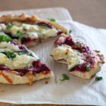 A photo of pizza topped with beet pesto, spinach, ricotta, mozzarella and chopped parsley.