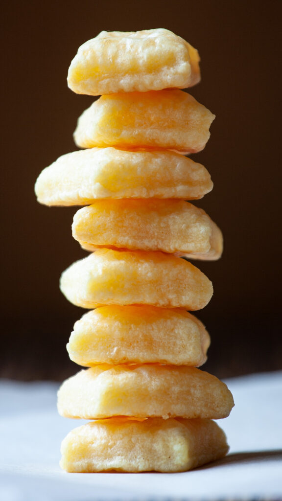 A photo of a stack of tiny square cheese crackers. The stack sits on a white piece of parchment paper.