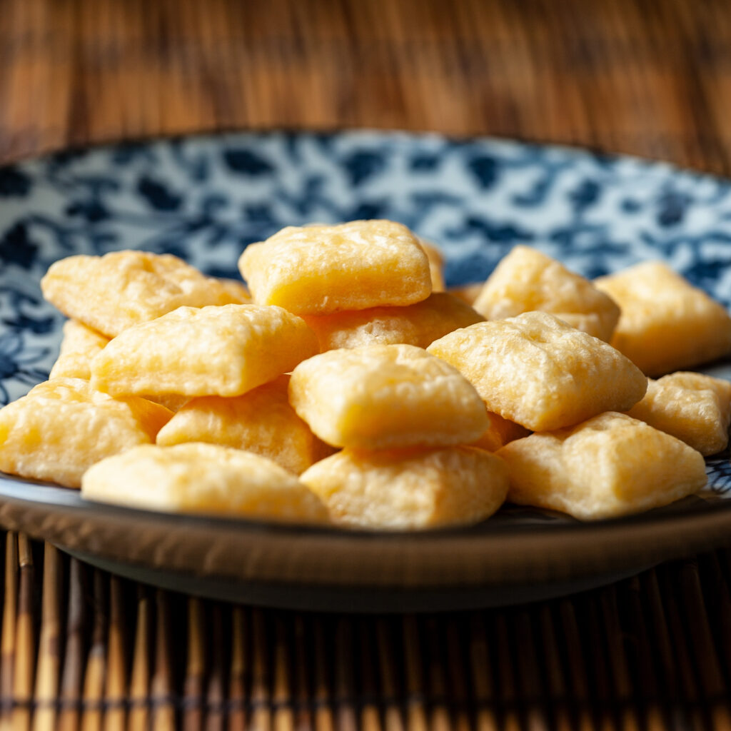 A three-quarter view photo of a blue and white plate, with many tiny square cheese crackers. The plate is on a bamboo placemat.