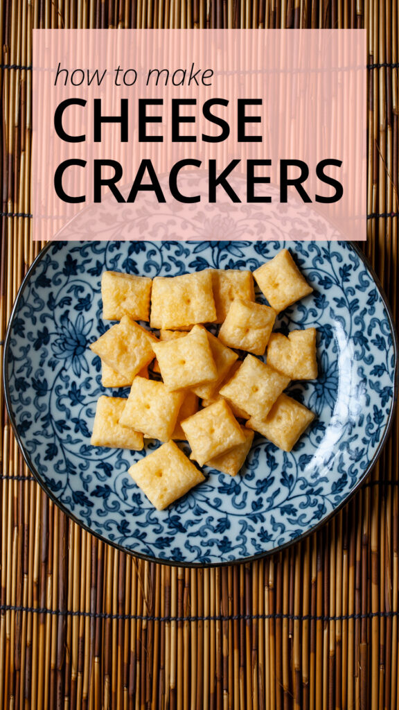 An overhead photo of a blue and white plate, with many tiny square cheese crackers. The plate is on a bamboo placemat.