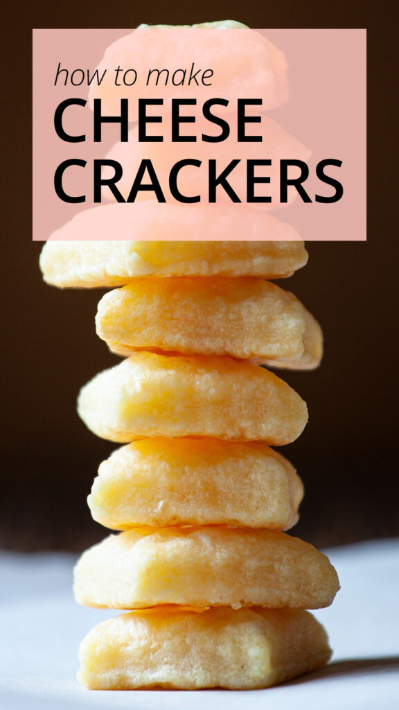 A photo of a stack of tiny square cheese crackers. The stack sits on a white piece of parchment paper.