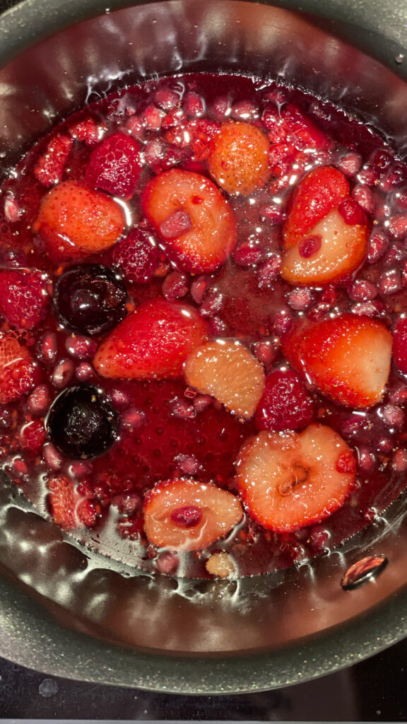 A photo of red berries cooking in syrup.