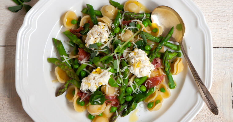 Orechiette pasta with fresh peas, ricotta, parmesan, olive oil, asparagus and prosciutto, on a plate with a spoon