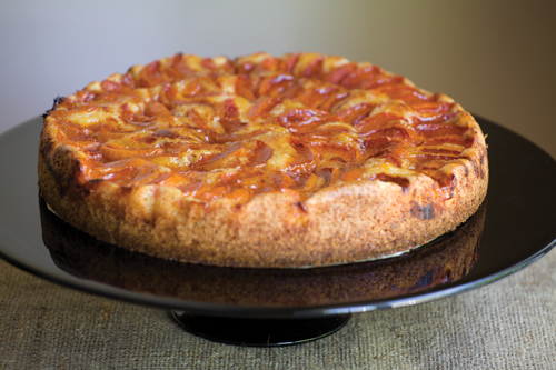 An apricot kuchen cake sits on a black cake stand