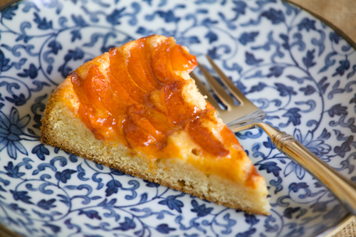 A slice of apricot kuchen cake sits on a blue plate, next to a fork.