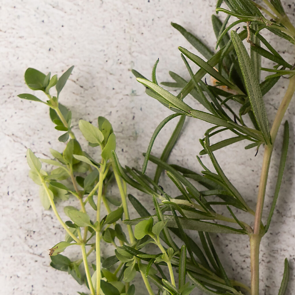 Springs of fresh rosemary and thyme rest on a surface.