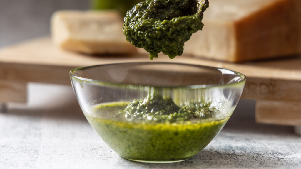 A glass bowl contains freshly made basil pesto.