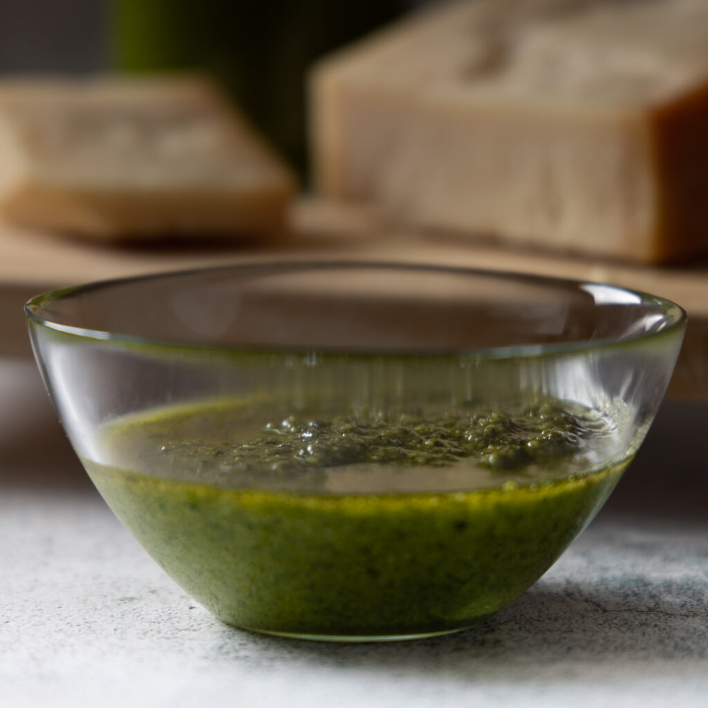 A glass bowl contains freshly made basil pesto.