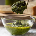 A glass bowl contains freshly made basil pesto.