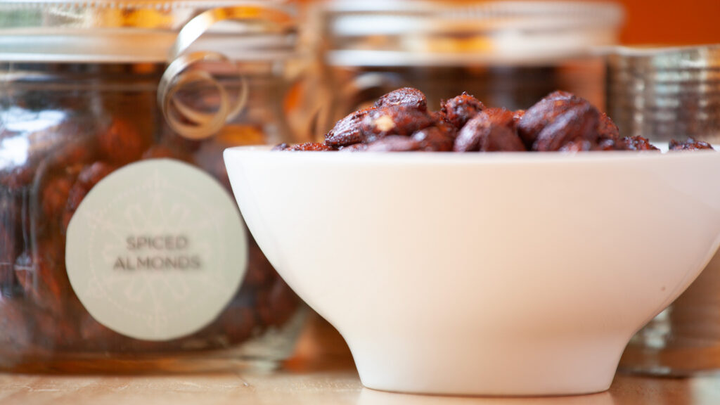 A white ceramic bowl containing holiday spiced nuts sit beside the bowl, and a wooden table.