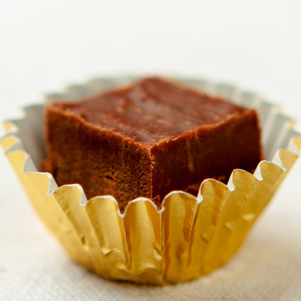 A single piece of chocolate fudge sits in a gold foil candy wrapper.