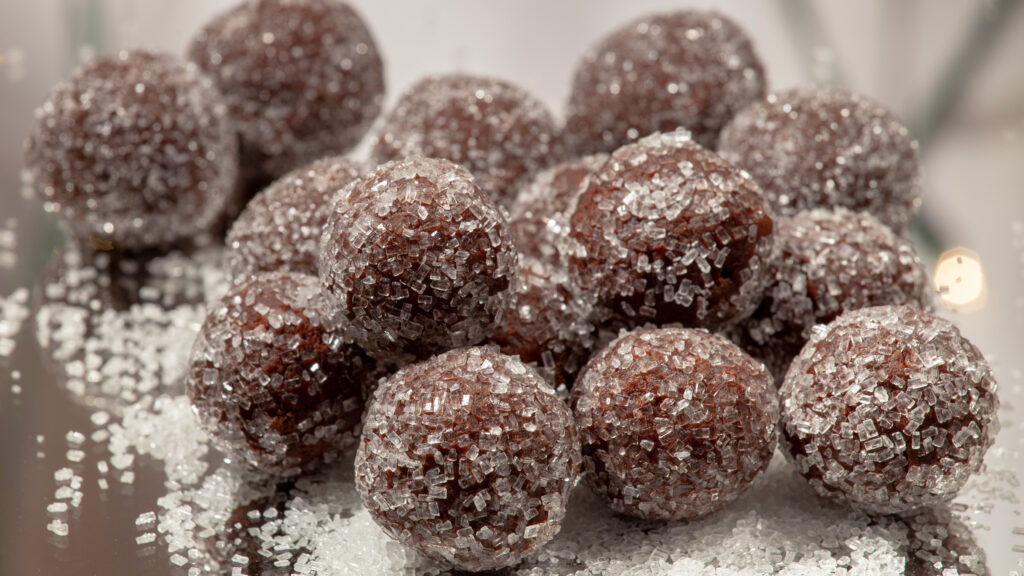 A pile of chocolate rum balls sits in a pile, on a mirrored surface.