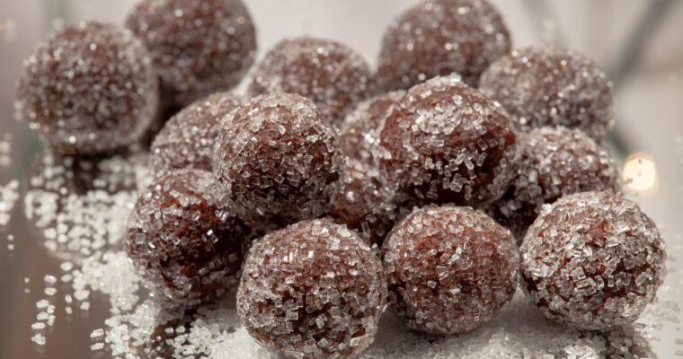 A pile of chocolate rum balls sits in a pile, on a mirrored surface.