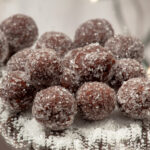 A pile of chocolate rum balls sits in a pile, on a mirrored surface.