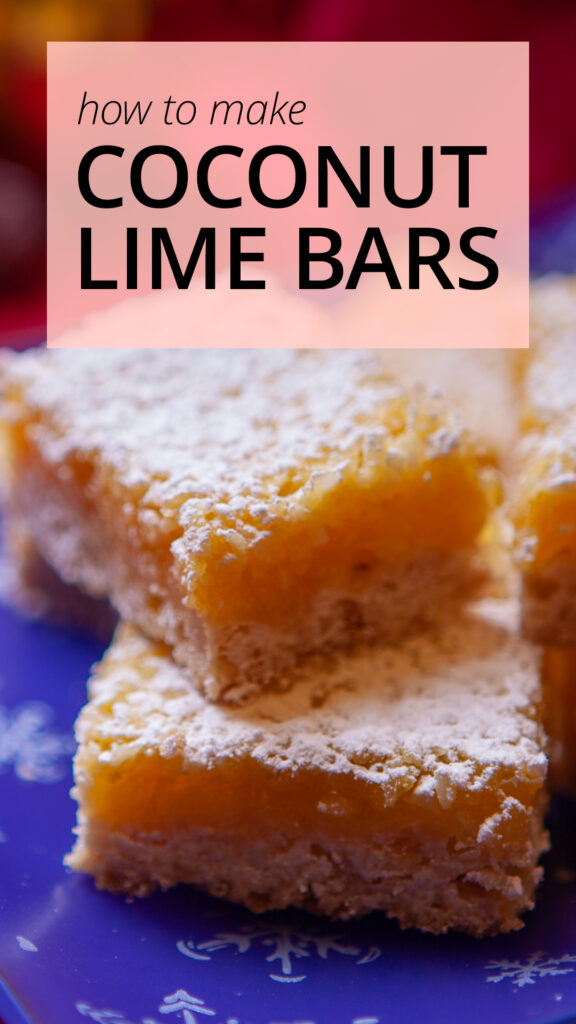 Coconut lime bars stacked on a blue glass plate decorated with snowflakes, sitting on a red tablecloth.