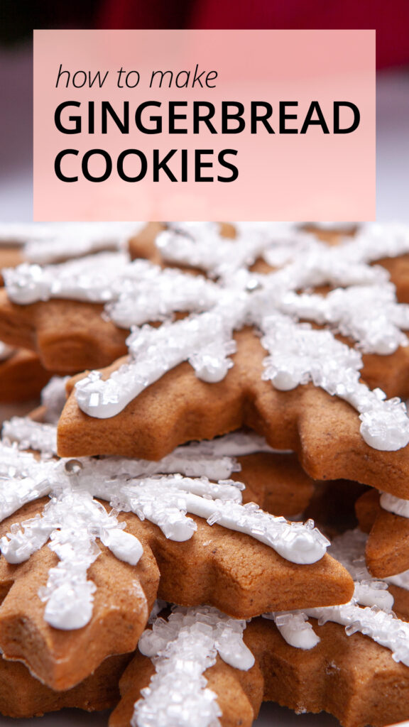 Snowflake shaped gingerbread cookies sit on a white plate. The cookies are decorated with white sparkle sugar and silver decorations.