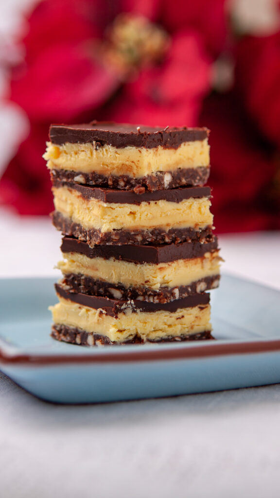 A stack of Nanaimo bars sits on a blue plate, with a poinsettia in the backbground.