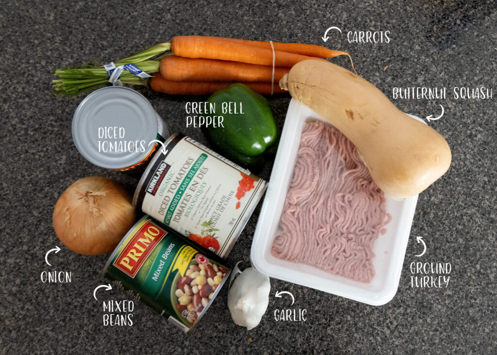 The ingredients for immune boosting turkey chili are on the counter, and feature 2 cans of mixed beans, a can of diced tomatoes, a butternut squash, bunch of carrots, one green pepper, head of garlic, one onion, and a package of ground turkey.