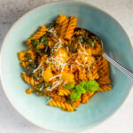 A bowl of sausage pasta with kale, yellow bell peppers, and spices.