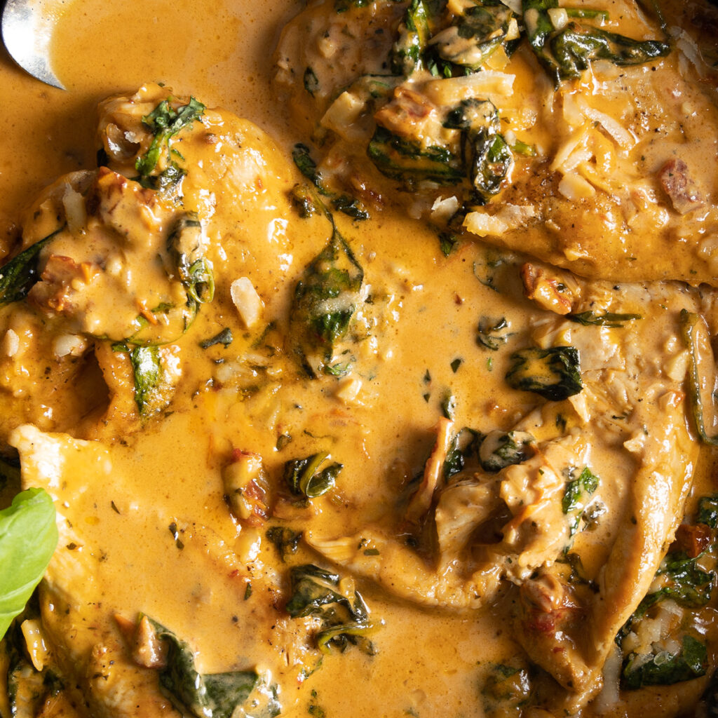 Juicy browned chicken breasts sit in a creamy parmesan sauce, with sundried tomatoes and spinach, in a cast iron pan. 