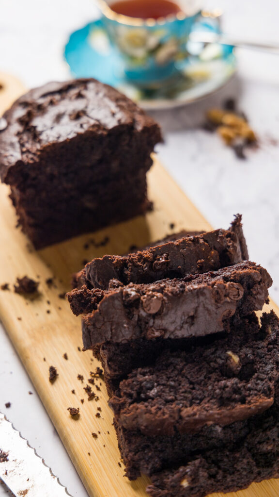 A loaf of chocolate banana bread sits on a wooden cutting board, partially sliced up.