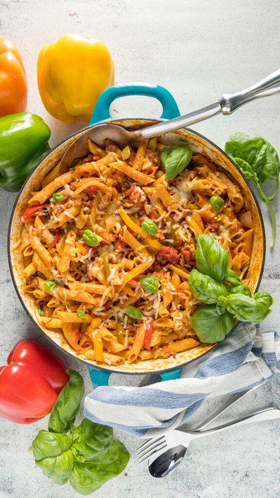 In a large skillet, penne pasta, Italian sausage, sliced bell peppers garnished with fresh basil.