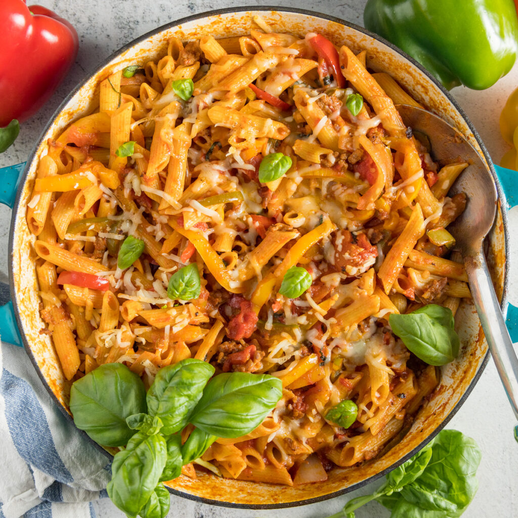 In a large skillet, penne pasta, Italian sausage, sliced bell peppers garnished with fresh basil.