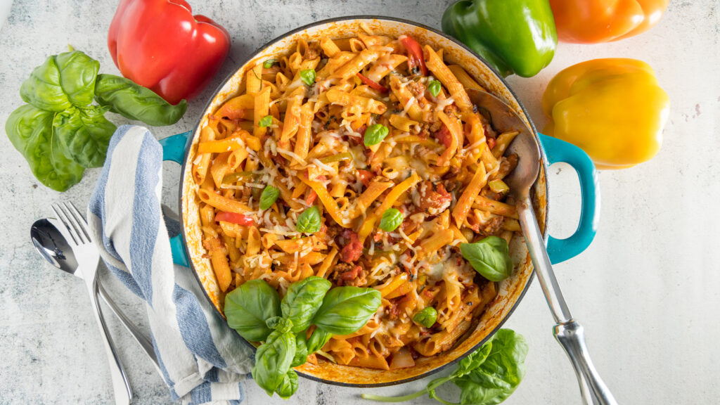 In a large skillet, penne pasta, Italian sausage, sliced bell peppers garnished with fresh basil.