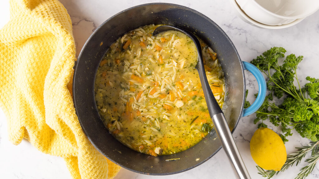 A pot of lemon chicken orzo soup, with a ladle, and a yellow towel.