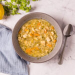 A bowl of lemon chicken orzo soup with carrots and celery.