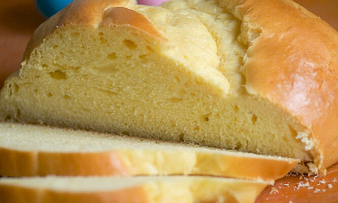 A rustic loaf of sweet Paska bread sits on a cutting board with colourful Easter eggs in the background.