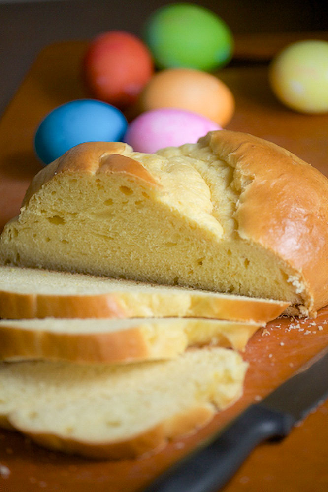 A rustic loaf of sweet Paska bread sits on a cutting board with colourful Easter eggs in the background.