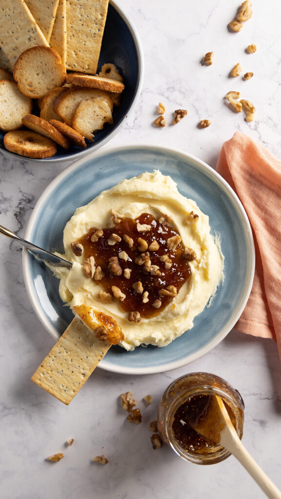 Whipped brie cheese in a bowl, topped with fig jam and chopped walnuts.