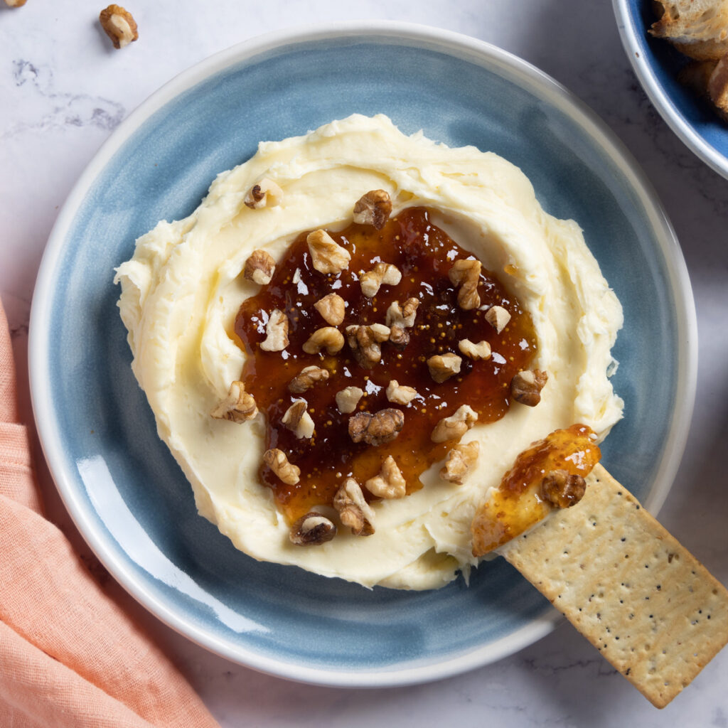 Whipped brie cheese in a bowl, topped with fig jam and chopped walnuts.