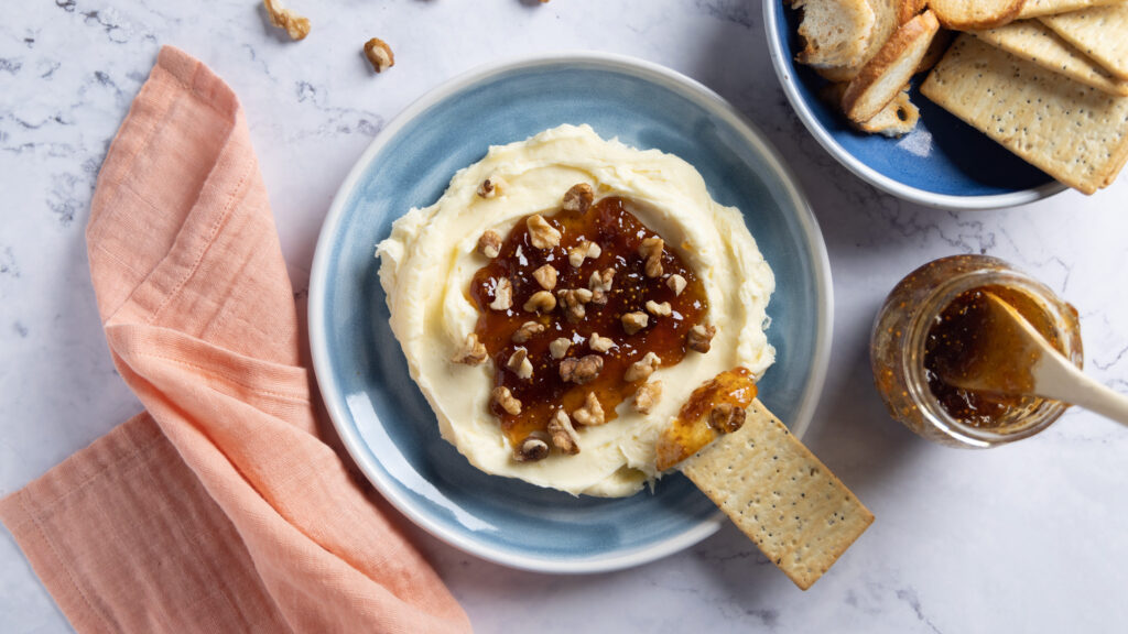 Whipped brie cheese in a bowl, topped with fig jam and chopped walnuts.