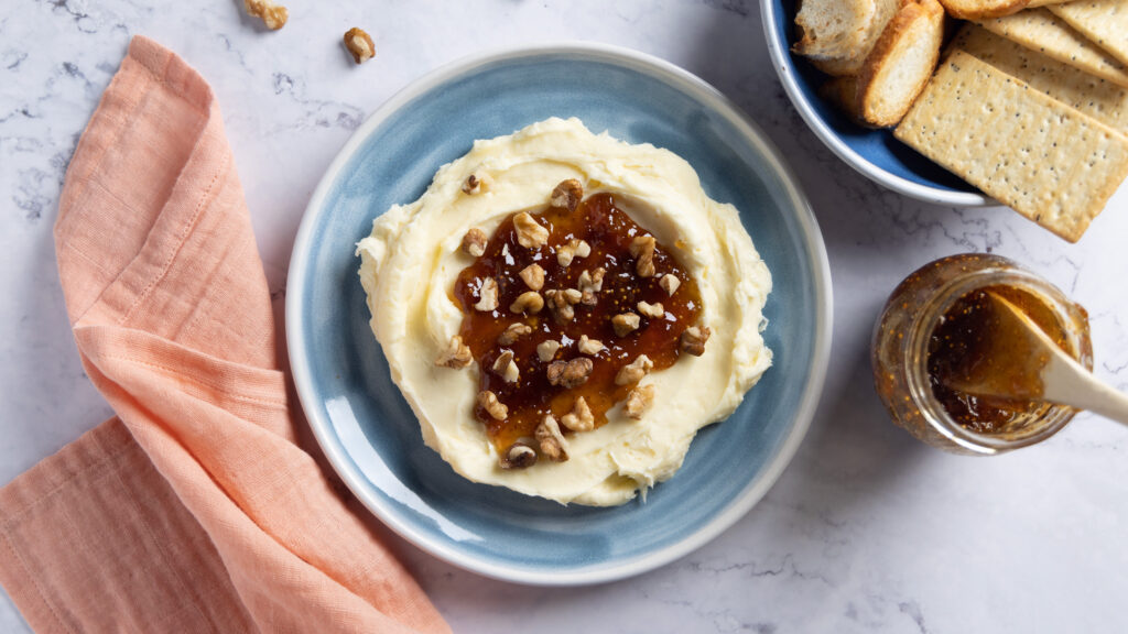 Whipped brie cheese in a bowl, topped with fig jam and chopped walnuts.