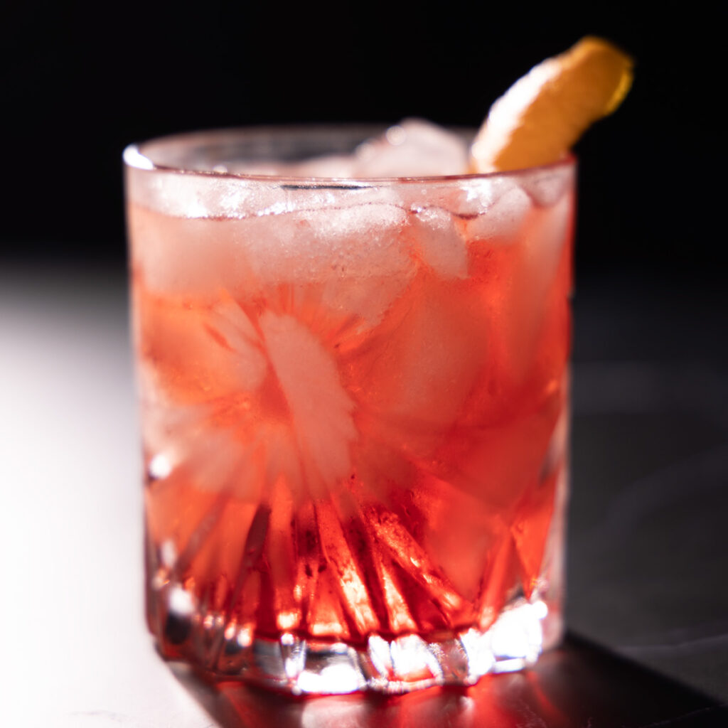 Crystal glasses contain a bright red non-alcholic cocktail garnished with orange peel.