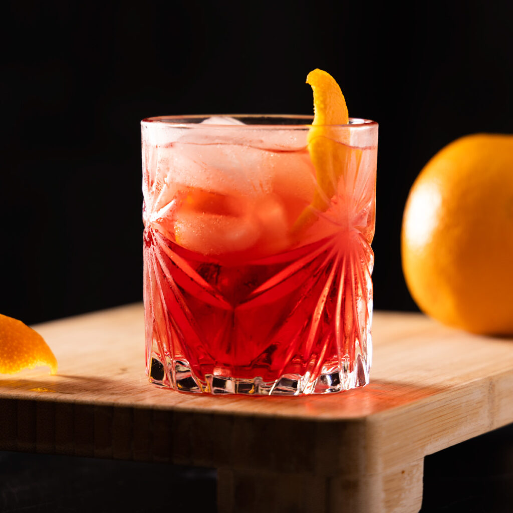 Crystal glasses contain a bright red non-alcholic cocktail garnished with orange peel.