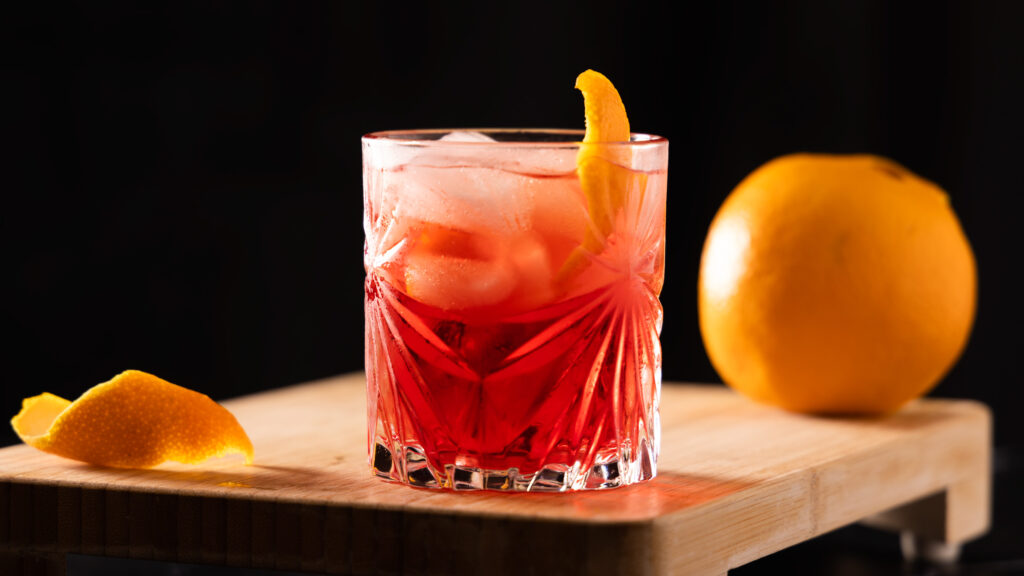 Crystal glasses contain a bright red non-alcholic cocktail garnished with orange peel.