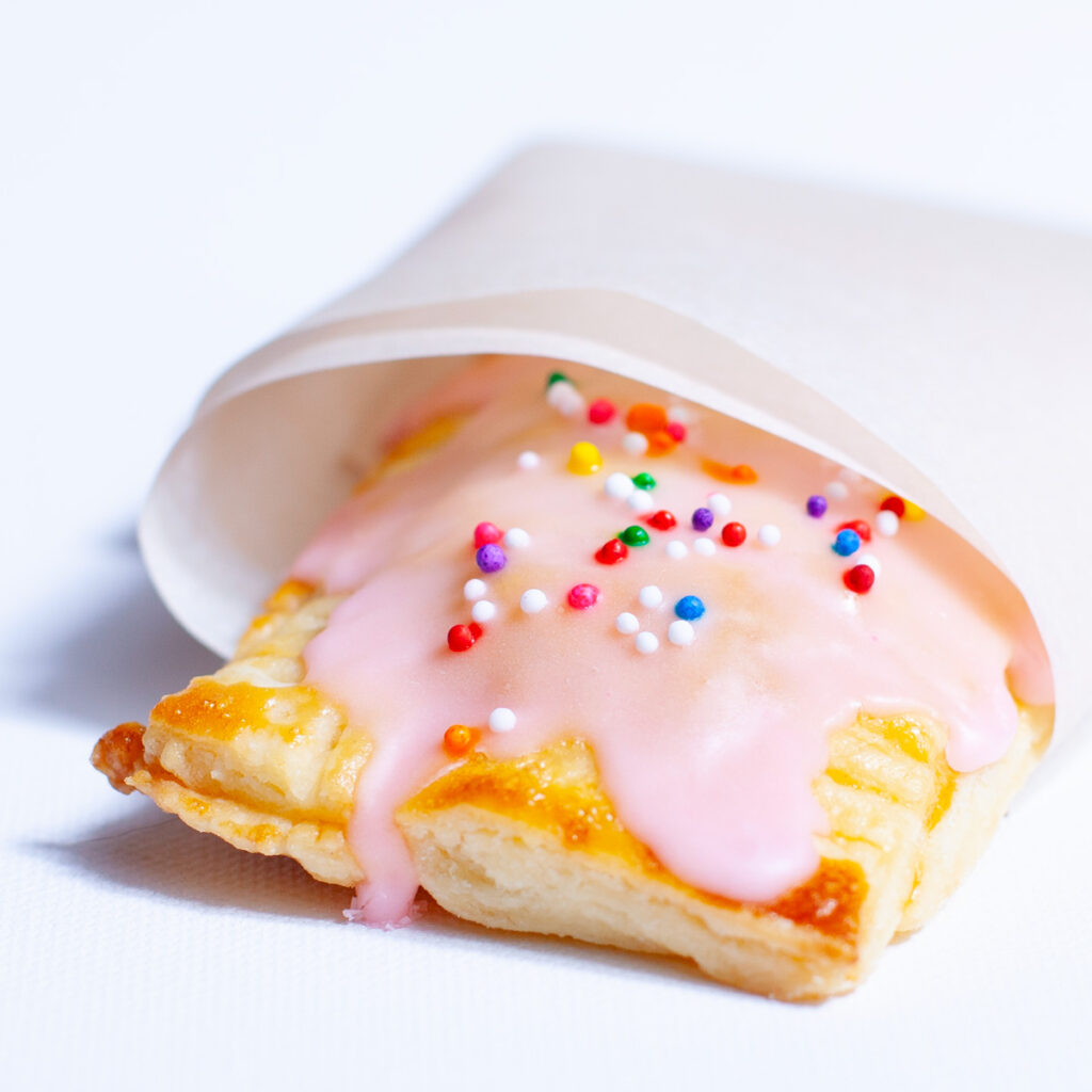 mini toaster pastries with pink icing, sprinkles, and wrapped in parchment paper.