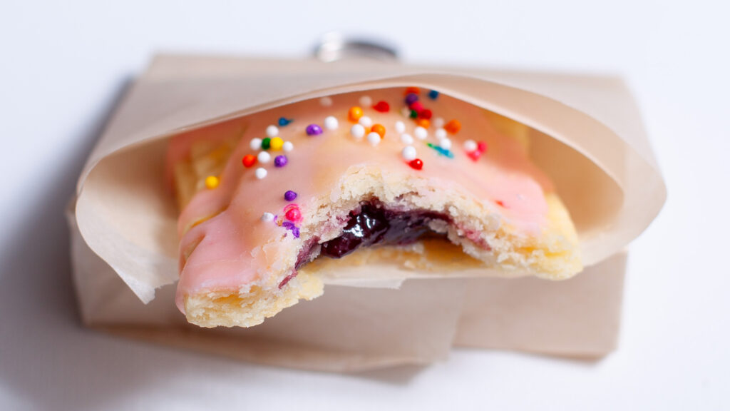 mini toaster pastries with pink icing, sprinkles, and wrapped in parchment paper.