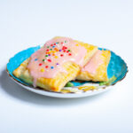 Mini toaster pastries with pink frosting and colorful sprinkles, on a blue plate.