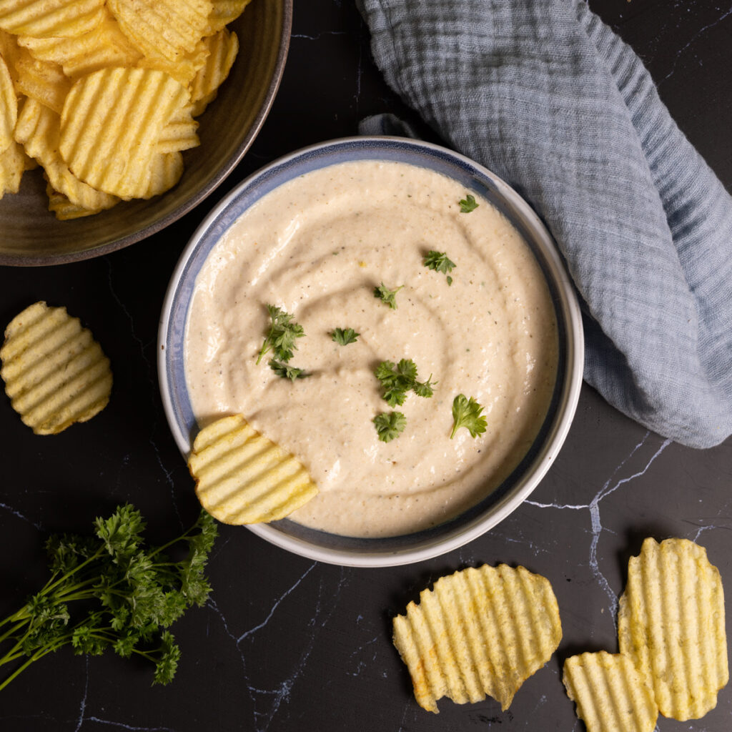 A bowl of onion dip sits on a counter with ripple potato chips on the side. 