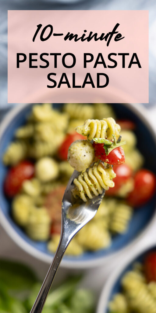 A pasta salad in a large salad bowl, with small tomatoes, basil pesto sauce, mini mozzarella balls, and chopped fresh basil. Hands are holding the bowl and a fork is lifting a bite of salad.