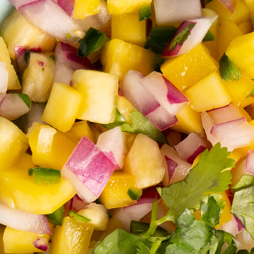 A close-up view of mango and pineapple salsa, with red onion and cilantro.